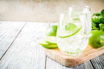 Summer sour drink, with lime and mint, homemade cocktail mojito in two glasses, white wooden background, with fresh limes, mint leaves, ice cubes, copy space
