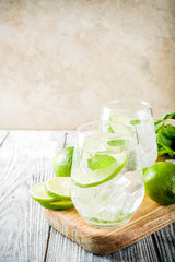 Summer sour drink, with lime and mint, homemade cocktail mojito in two glasses, white wooden background, with fresh limes, mint leaves, ice cubes, copy space