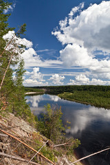 Wood and white clouds in the blue sky reflected in the mirrored water of a lake