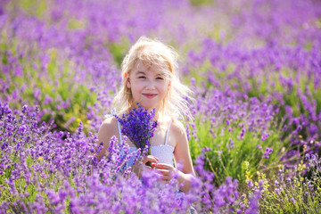 Fototapeta na wymiar Blonde girl in the colour dress sitting on the field o lavander with a small bouqet in her hands