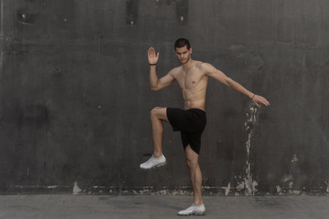 Young athlete man, naked torso, running against a gray wall