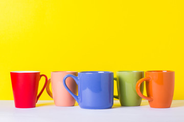 A lot of multicolored cups of coffee or tea on a yellow background. The concept of a friendly company, a large family, meeting friends for a cup of tea or coffee.