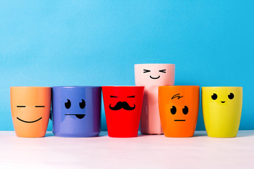 A lot of multi-colored cups with funny faces on a blue background. The concept of a friendly...