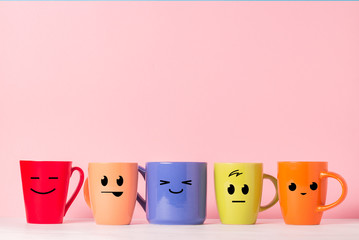 A lot of multicolored cups with funny faces on a pink background. The concept of a friendly company, a big family, meeting friends for a cup of tea or coffee, father's day, office, boss day.
