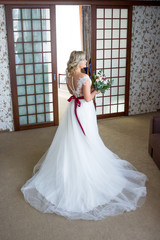 beautiful bride with hair and makeup suits wedding dress with lacing at the back and a wedding bouquet in the background.