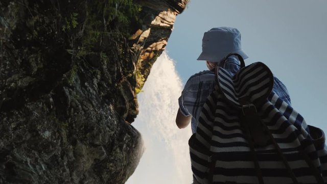 A tourist stands under Steinsdalsfossen waterfall takes a photo , above it hangs a rock and runs a stream of water. Low angle shot