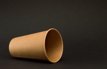 empty paper cup for coffee lies on its side on a black background, fell glass