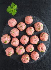 Uncooked raw meatballs on black stone cutting board