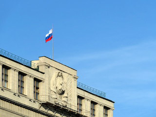 Fototapeta na wymiar Russian flag on the Parliament building in Moscow against blue sky. Facade of State Duma of Russia with soviet coat of arms