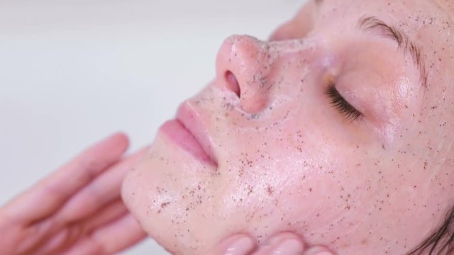 Woman puts a scrub on the face lying in the bathroom. Face close-up. White background.