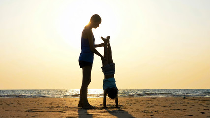 Silhouette of mother with daughter doing gymnastic on the beach at sunset
