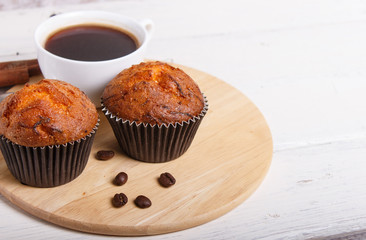 two carrot muffins with cup of coffee on wooden kitchen board on white wooden background