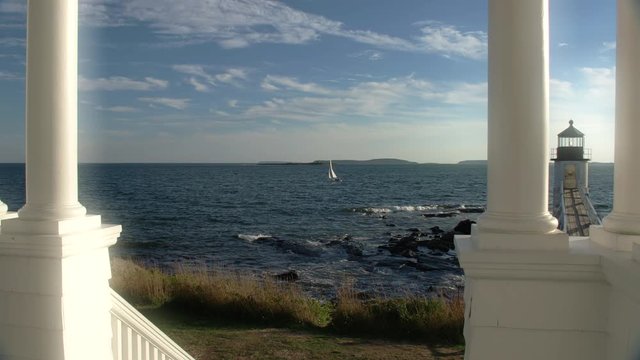 Beautiful view of coastal Maine lighthouse with ocean view looking out past white columns and deck railing on a porch