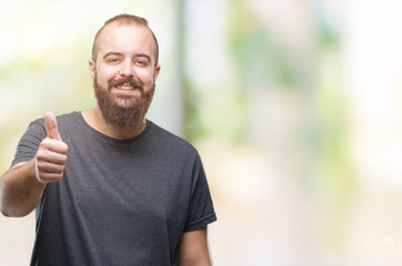 Young caucasian hipster man over isolated background doing happy thumbs up gesture with hand. Approving expression looking at the camera with showing success.