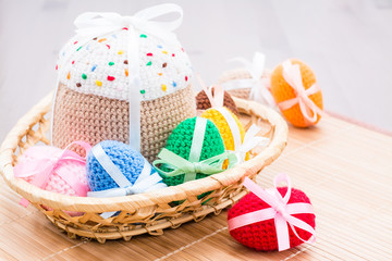 Knitted Easter eggs and Easter cake in a wicker basket on a wooden table