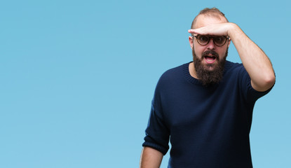 Young caucasian hipster man wearing sunglasses over isolated background very happy and smiling looking far away with hand over head. Searching concept.