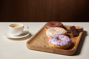 glazed doughnuts with sprinkles on wooden cutting board near cup of coffee