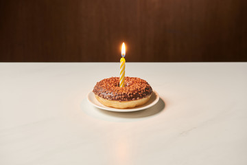 burning candle in middle of sweet doughnut with icing and sprinkles on white table
