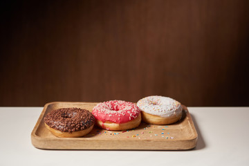 tasty donuts with icing and sprinkles on wooden cutting board
