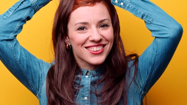 Funny changing style and emotions. Beautiful woman in classic wig with long brown hair positively taking off it. Girl turns stylish redhead pixie haircut. Female casual fashion on yellow background.