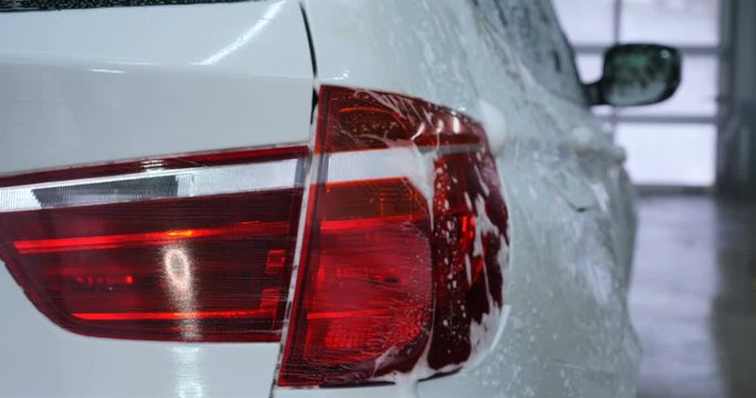 Professional guy (man) in a car wash washes a very dirty car using Karcher and splashes foam, wipes the car with a sponge. Concept of: Car wash, Wash accessories, Under high pressure.