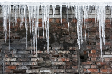 Icicles hanging from roof of the building, water drips from them/copy space/fall icicles,sudden warming,сold winter, poor thermal insulation,ice stalactite, formation of icicles,winter weather concept
