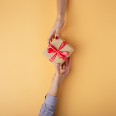 man gives a girl a gift from hand to hand, box wrapped in decorative paper on orange background, the concept of holidays, top view