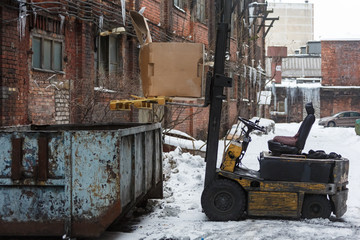 Fototapeta na wymiar Yellow loader loads garbage in large trash can/the driver left his vehicle and left for help, industrial machinery, factory territory, slippy road, old equipment, frost and winter concept.
