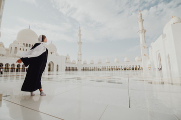 Traveling by United Arabic Emirates. Young woman in traditional abaya standing in the Sheikh Zayed Grand Mosque, famous Abu Dhabi sightseeing.