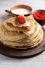 Stack of russian thin pancakes blini with red caviar and fresh sour cream