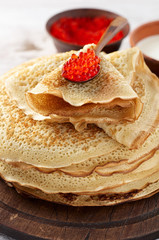 Stack of russian thin pancakes blini with red caviar and fresh sour cream
