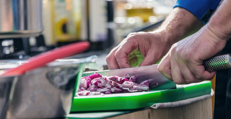 Close up of unrecognizable cook cutting onions and other vegetables with chef knife while working
