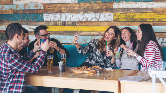 Group of friends having fun drinking bear and eating pizza at bar restaurant while taking selfie and pictures