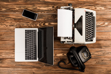top view of typewriter, laptop, rotary dial telephone and smartphone on wooden table