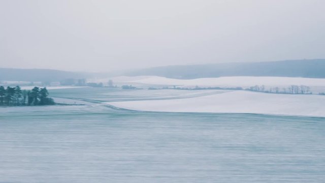 Cinematic view through the window of a fast TGV ICE train over the frozen covered with snow French hills and villages early in the morning on the cold snowy winter - 4K UHD footage