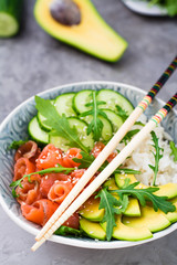 Salmon poke with avocado,  arugula and cucumber in a bowl and chopsticks