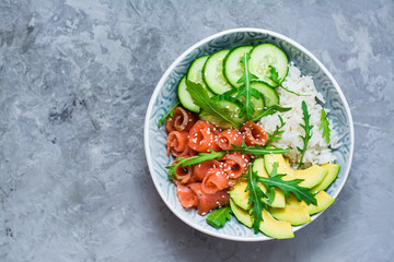Salmon poke with avocado, arugula and cucumber in a bowl. Top view. Copy space
