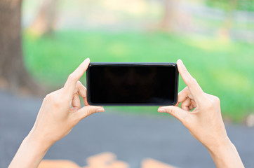 Hand holding smartphone with black screen on nature background.