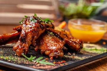 The concept of Indian cuisine. Baked chicken wings and legs in honey mustard sauce. Serving dishes in the restaurant on a black plate. Indian spices on a wooden table. background image.