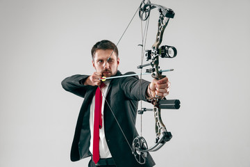 Businessman aiming at target with bow and arrow isolated on gray studio background. The business,...