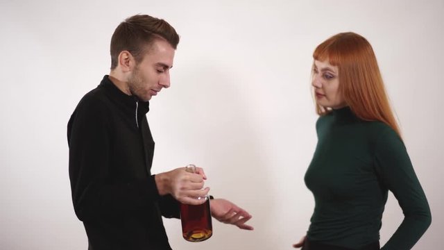 Emotional caring loving wife leaning to her depressed alcoholic husband and feeling desperate while trying to take a bottle of alcohol from him.