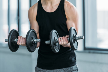 cropped shot of muscular young man exercising with dumbbells in gym