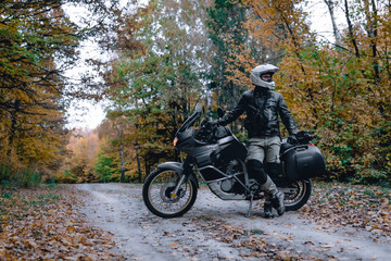Fototapeta na wymiar Biker man in leather jacket and black tourist motorcycle with side bags. wallpaper concept, enduro advetnture, space for text, autmn season