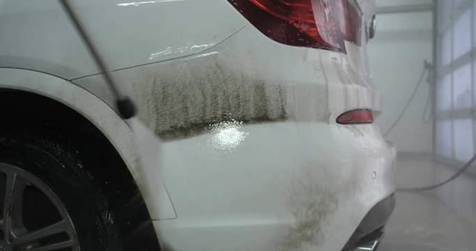 Professional guy (man) in a car wash washes a very dirty car using Karcher and splashes foam, wipes the car with a sponge. Concept of: Car wash, Wash accessories, Under high pressure.