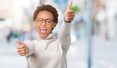 Young beautiful african american woman wearing glasses over isolated background approving doing positive gesture with hand, thumbs up smiling and happy for success. Looking at the camera