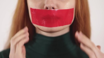 Young upset crying woman with long hair put red tape on her mouth with hands - Powered by Adobe