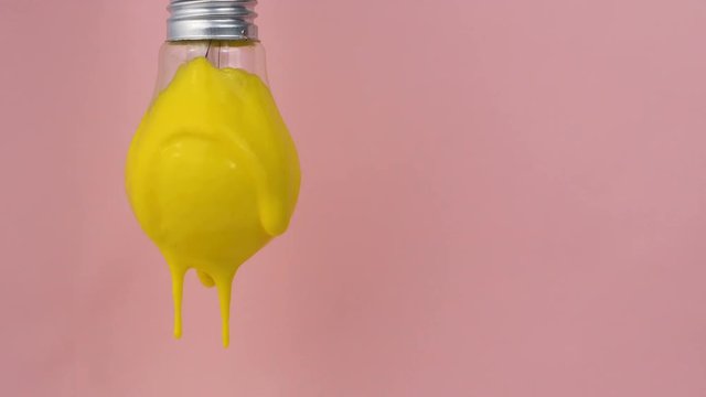Lightbulb in yellow paint on pink background. Yellow paint dripping from the lamp.