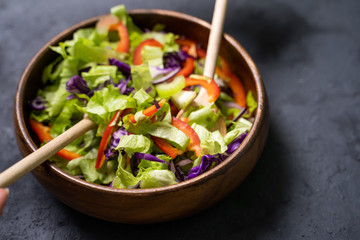 Fresh vegetables salad with purple cabbage, white cabbage, lettuce, carrot in dark clay bowl on black background.