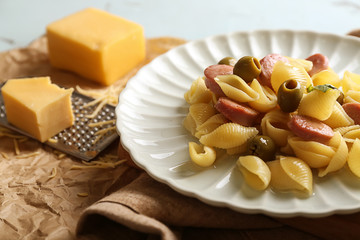 Plate with delicious macaroni, vegetables and cut sausages on table