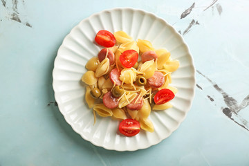 Plate with delicious macaroni, vegetables and cut sausages on table